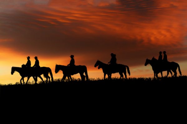 Sonnenuntergang Sillhouette von sieben Reitern mit Hüten auf Pferden